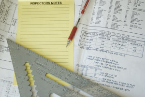 Inspection notes, ruler, and red pen atop construction plans